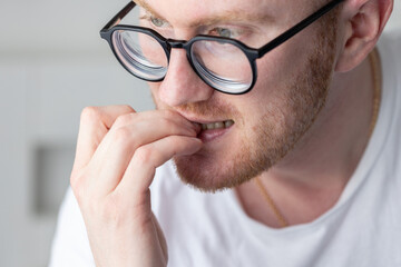 Portrait of brooding man in glasses chewing on his fingernails. Fingernail biting. - Powered by Adobe