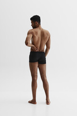 Fototapeta premium Back view. Young African-American man with relief strong back, muscular body standing in boxers isolated on white background. Back pain reduction. Concept of sport, body care, health, fitness