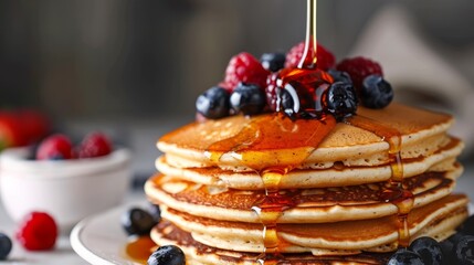 A stack of whole grain pancakes topped with fresh berries and maple syrup, close-up to showcase the natural syrup flow, studio lighting