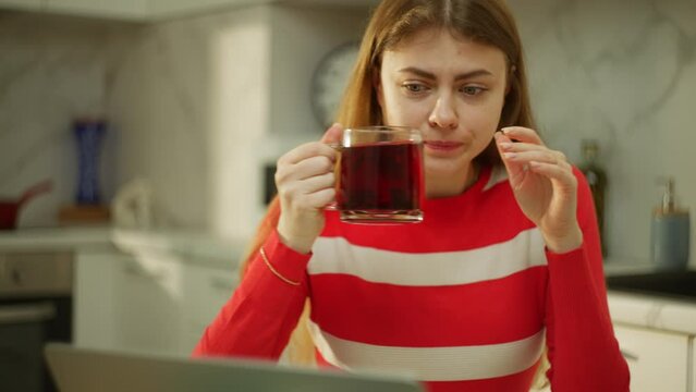 Thoughtful woman drinks tea from a large mug in front of a laptop. When working at home, there is always time for a break. High quality 4k footage