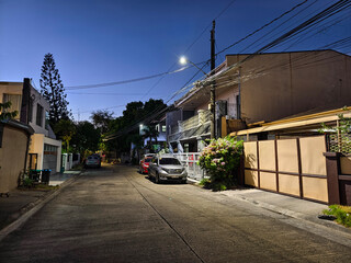 Las Pinas, Metro Manila, Philippines - April 28, 2024: Evening scene on a typical suburban street in BF Resort Village with houses and parked cars under a vibrant sunset sky.
