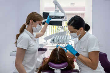 female dentist and a female assistant in a special uniform treat the teeth of a female patient.