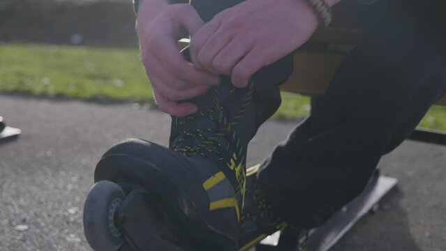 Close up young man tying inline roller blade skates laces, golden hour evening sunset