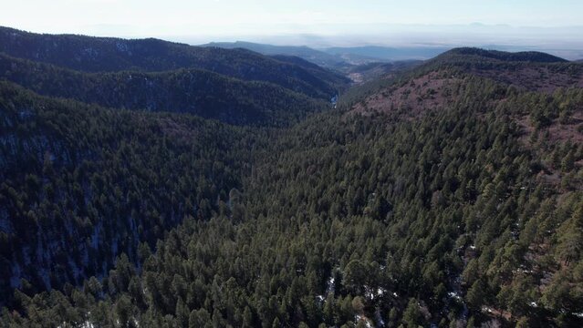 Aerial view of a New Mexico mountain valley pulls back and tilts to reveal a distant horizon