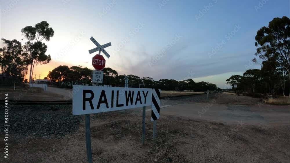 Poster a railway line crossing a road with a passing train in a time-lapse shot.