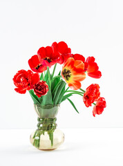 A bouquet of lush red tulips in vintage glass vase on the table on light grey background. Business card of flower shop with copy space. Invitation postcard. International women's day. Valentine's day