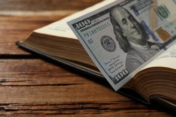 Open Bible with money on wooden table, closeup