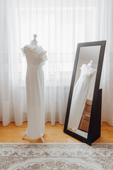 A white dress is standing in front of a mirror. The dress is long and elegant, and the mirror is...