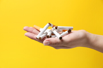 Stop smoking. Woman holding broken cigarettes on yellow background, closeup