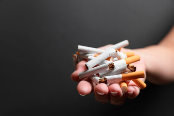 Stop smoking. Woman holding broken cigarettes on black background, closeup. Space for text