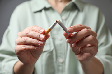 Stop smoking. Woman holding broken cigarette on grey background, closeup
