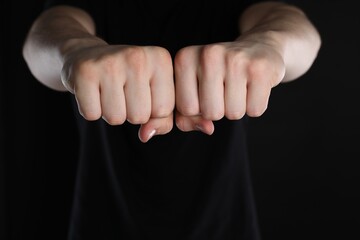Man showing fists with space for tattoo on black background, closeup