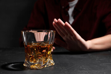 Alcohol addiction. Woman refusing glass of whiskey at dark textured table, closeup