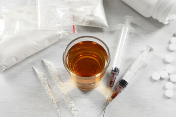 Alcohol and drug addiction. Whiskey in glass, syringes, cocaine and pills on white table