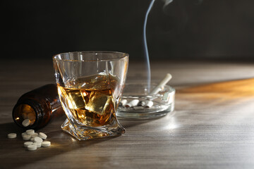 Alcohol addiction. Whiskey in glass, pills and cigarettes on wooden table, space for text