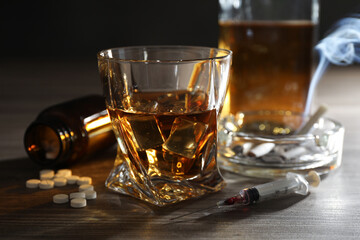 Alcohol and drug addiction. Whiskey in glass, syringe, pills and cigarettes on wooden table