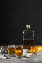 Alcohol and drug addiction. Whiskey in glasses, syringes, pills and cocaine on grey table