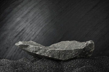 Presentation of product. Stone podium on black sand against dark textured background. Space for text © New Africa