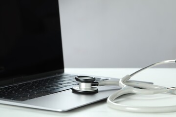 Modern laptop and stethoscope on white table, closeup. Space for text