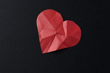 Red crumpled paper heart on black background, top view. Breakup concept