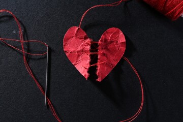 Halves of torn paper heart connected by thread on black background, flat lay. Relationship problem concept