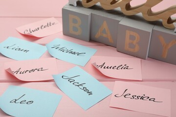 Cubes with word Baby and paper stickers with different names on pink wooden table. Choosing baby's name