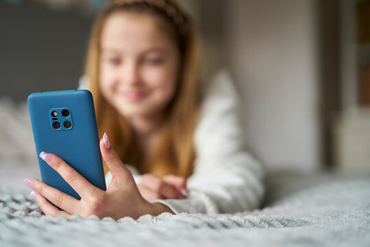 Smiling Teenage Girl With Painted Nails Lying On Bed At Home Using Moblie Phone