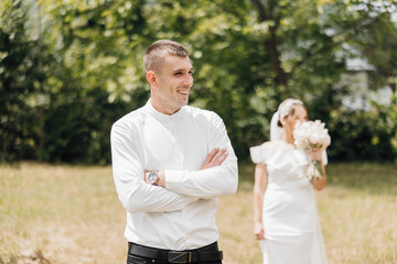 A man and a woman are standing in a field, with the man wearing a white shirt and the woman holding a bouquet of flowers. The scene is likely a wedding, as the woman is wearing a white dress