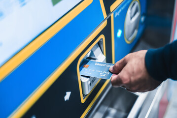 Close-up of a hand inserting a credit card into a public transportation ticket vending machine.