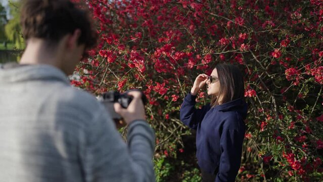 Photographer with digital camera do photo shoot with woman near blooming shrub