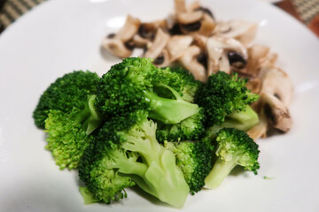 close up of raw broccoli vegetables with mushroom at the back on a white plate