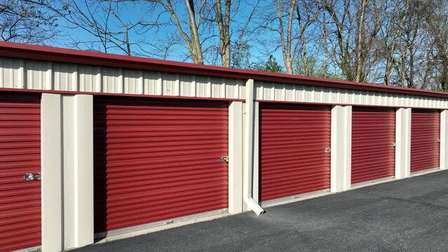 Red Colored Self Storage Unit Buildings or Warehouse Temporary Storage in spring.  American suburb garage during sunny day. Aerial passing by.