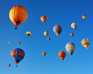 Hot air balloons in various colors floating in a clear blue sky.