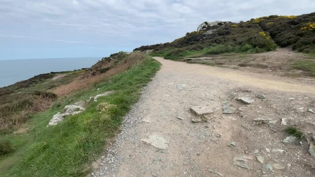 Scenic walking trail along the rugged coastline of Howth, Ireland, leading toward a lighthouse with rocky cliffs, green vegetation, and views of the Irish Sea.