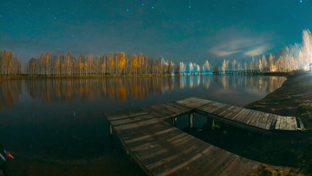 Slider shot of Deep Night Stars Above Lake. reflection on water surface wide angel, tranquil motion. Autumn River Landscape stars. Natural Starry Sky Landscape. Wooden Pier. Autumn Forest woods lake