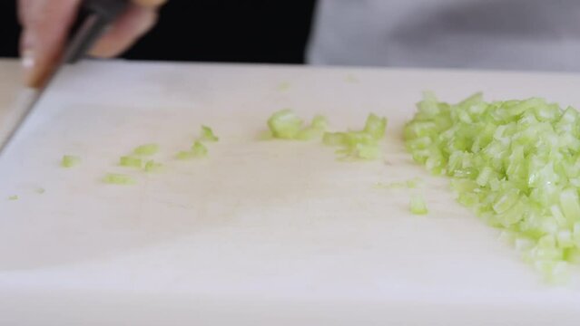 The cook cuts celery stalks with a large kitchen knife into small slices.