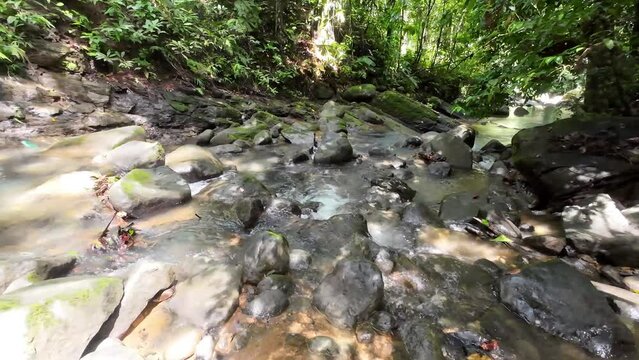 Gentle tracking shot through a picturesque river with majestic waterfall and large stones 4K resolution