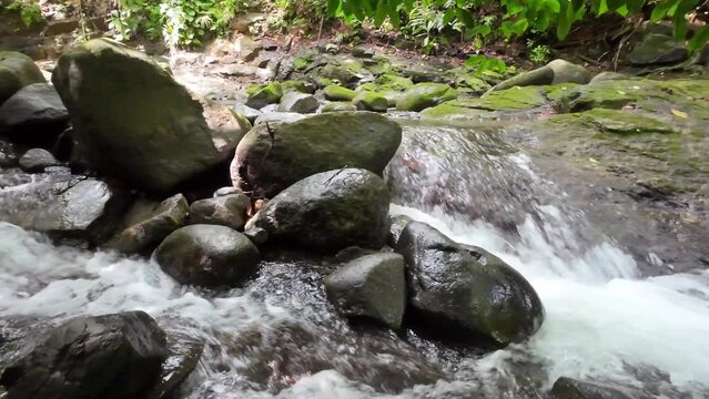 Gentle tracking shot through a picturesque river with majestic waterfall and large stones 4K resolution