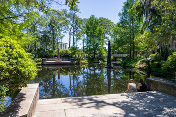 a beautiful spring landscape in the Sculpture Garden at New Orleans City Park with a lake, lush green trees, grass and plants, sculptures, people and blue sky in New Orleans Louisiana USA