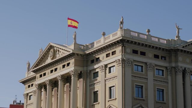 Spanish flag fluttering on grand Barcelona building, blue sky backdrop, stationary shot