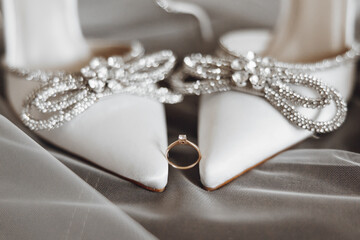 A pair of white shoes with a diamond ring on the left shoe. The ring is placed on the shoe to symbolize a wedding