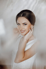 A woman is posing for a picture with her hair up and her hands on her face. She is wearing a white dress and has her hair in a bun. The photo has a soft, romantic feel to it