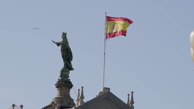 Spanish flag waving next to a statue under clear blue skies in Barcelona