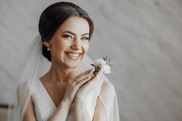 A woman is smiling and holding a flower in her hand. She is wearing a wedding dress and a veil
