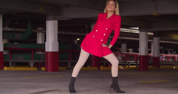 In the midst of city life, a young girl of Hispanic origin graces a parking garage, dressed in a short red attire.