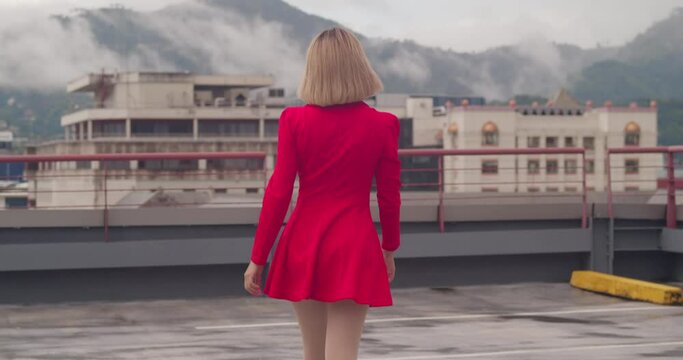 A rooftop in the bustling city becomes the stage for a young Hispanic girl, walking adorned in a short red dress.