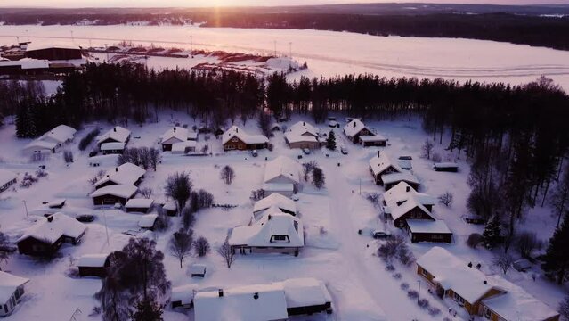 Aerial winter sunset over snow-covered neighborhood next to a frozen lake and a forest