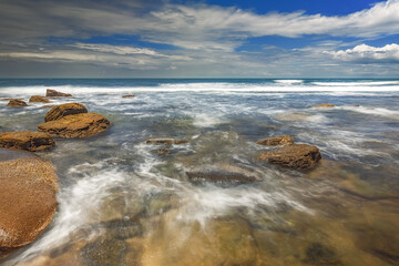 Obraz premium Cean waves crashing against numerous stones in a vibrant blue sea in Moffat Beach, Queensland