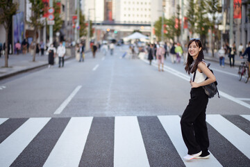Explore urban vibes with a happy Asian woman at a city crosswalk, showcasing a mix of style, joy, and the pulse of local life.