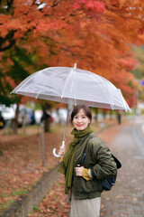 Asian woman with an umbrella embraces the joy of fall amid the rain. A cheerful and happy portrait capturing the beauty of nature's colors.